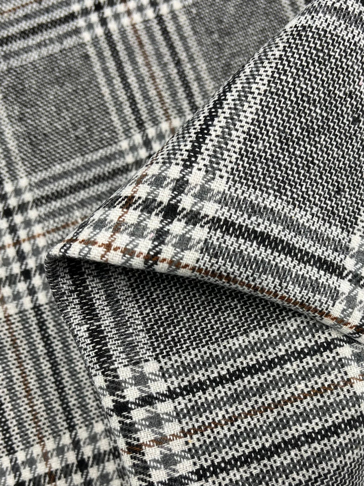 Close-up of a folded piece of Wool Flannel - Nuthatch Plaid from Super Cheap Fabrics, featuring a high-quality blend in black, white, and gray. This fabric showcases a classic plaid pattern with interwoven lines, demonstrating a textured appearance perfect for winter pants. Light and shadow create depth, highlighting the weave's intricacy across its 150cm width.