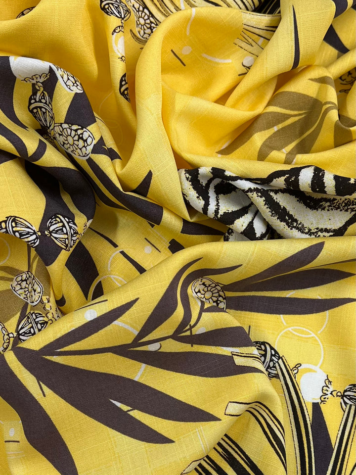 A close-up image of vibrant yellow Bamboo Rayon - Pina Colada - 150cm from Super Cheap Fabrics, featuring intricate black and white designs, including abstract patterns, florals, and geometric shapes. The lightweight fabric is slightly wrinkled and gathered, creating a dynamic and textured appearance ideal for face masks.