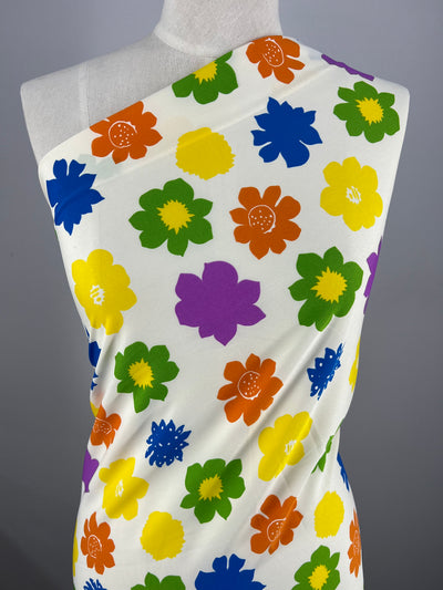 A white dress mannequin is draped with a designer fabric featuring a vibrant, colorful pattern of large flowers in shades of yellow, orange, green, purple, and blue. The Deluxe Print - Flower Spread - 150cm by Super Cheap Fabrics is wrapped to cover the mannequin's upper body in an off-the-shoulder style.