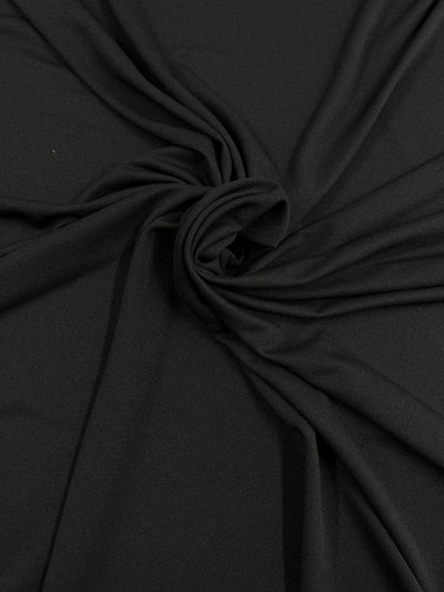 A close-up of smooth black fabric with a gathered, twisted design at the center, creating a textured, ruched pattern. The folds radiate outward, giving a sense of motion and fluidity. The lightweight fabric appears soft and slightly shiny, making it an elegant garment accent. This is the Lining - Knit Lining - Black - 140cm by Super Cheap Fabrics.