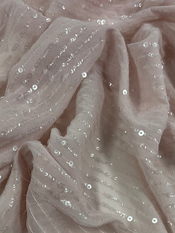 A close-up image of soft baby pink fabric with small sequins sewn in rows. The medium weight fabric is slightly wrinkled, giving it a textured appearance. The sequins catch the light, adding a subtle sparkle to the Evening Sequin - Baby Pink - 150cm material by Super Cheap Fabrics.